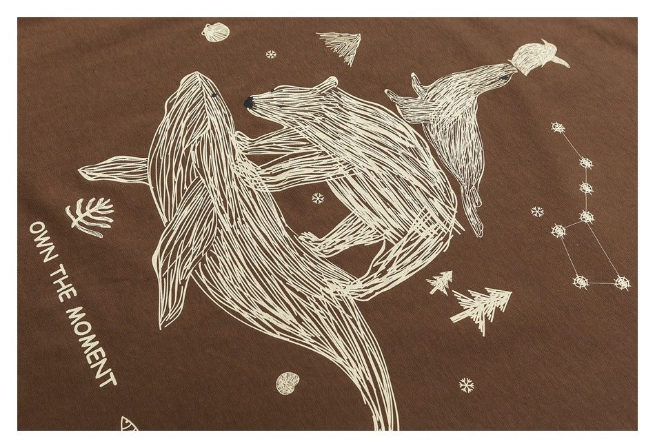 Close-up of brown fabric with a cream whale and celestial illustration, plus the printed words “OWN THE MOMENT.”