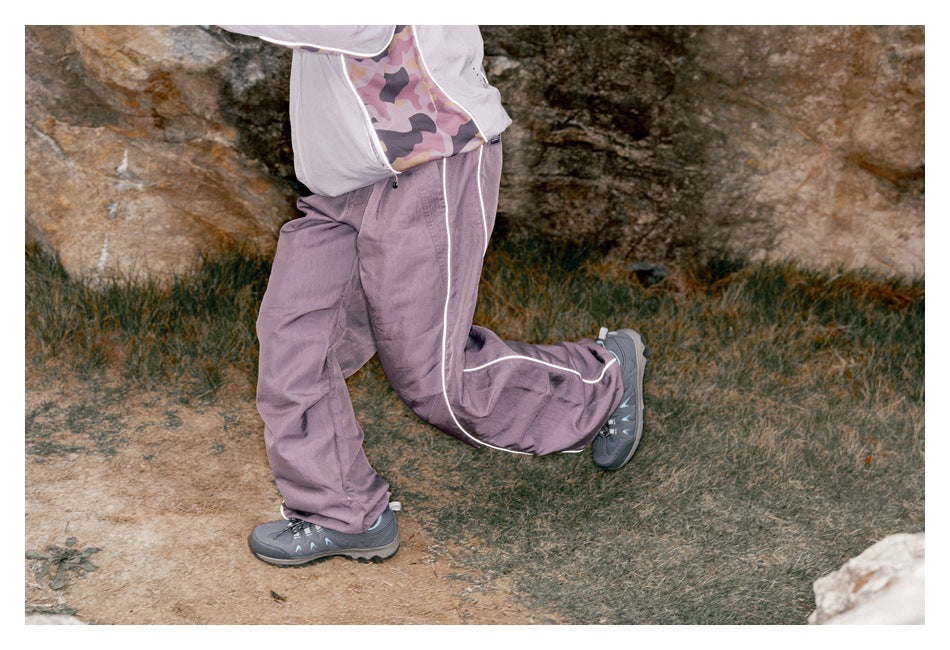 Side view of a model wearing loose muted lavender pants with white piping while stepping outdoors.