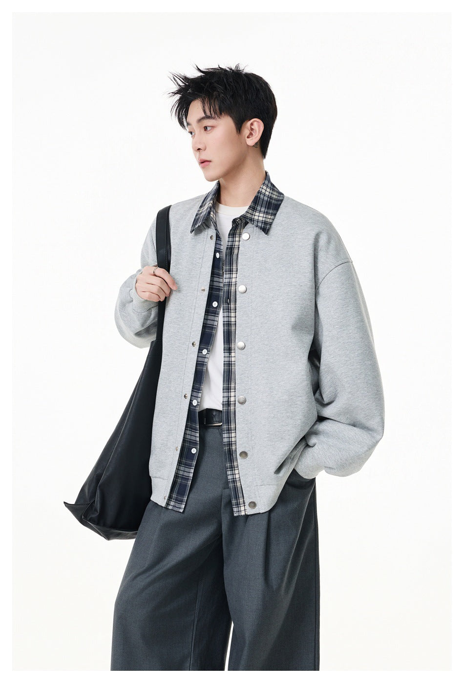 Model wearing a light gray snap-front jacket over a dark plaid shirt, with a black shoulder bag.