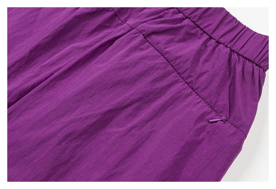 Close-up of purple pants showing an elastic waistband, stitched panel, and small zipper pull.