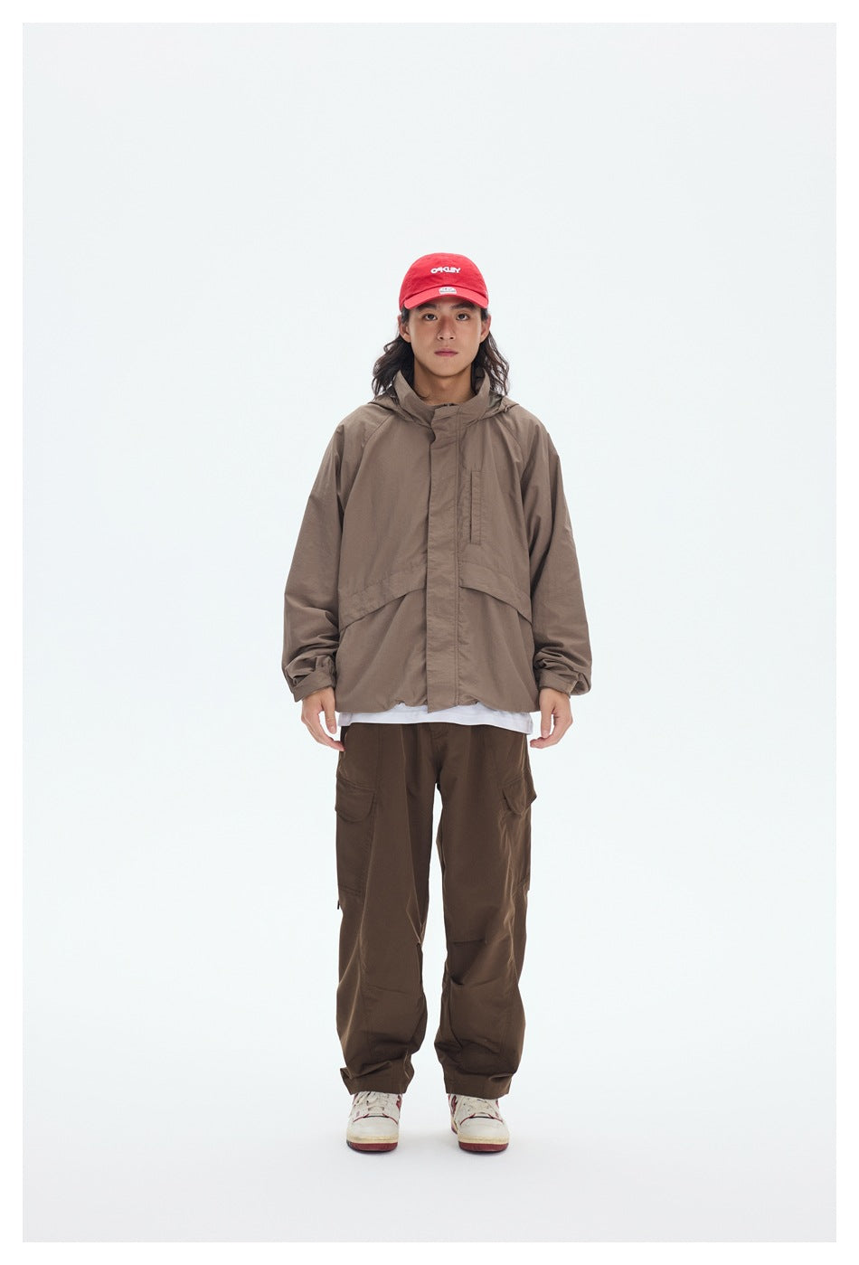 Model in a taupe hooded jacket with a covered front closure and dark brown cargo pants, facing forward.