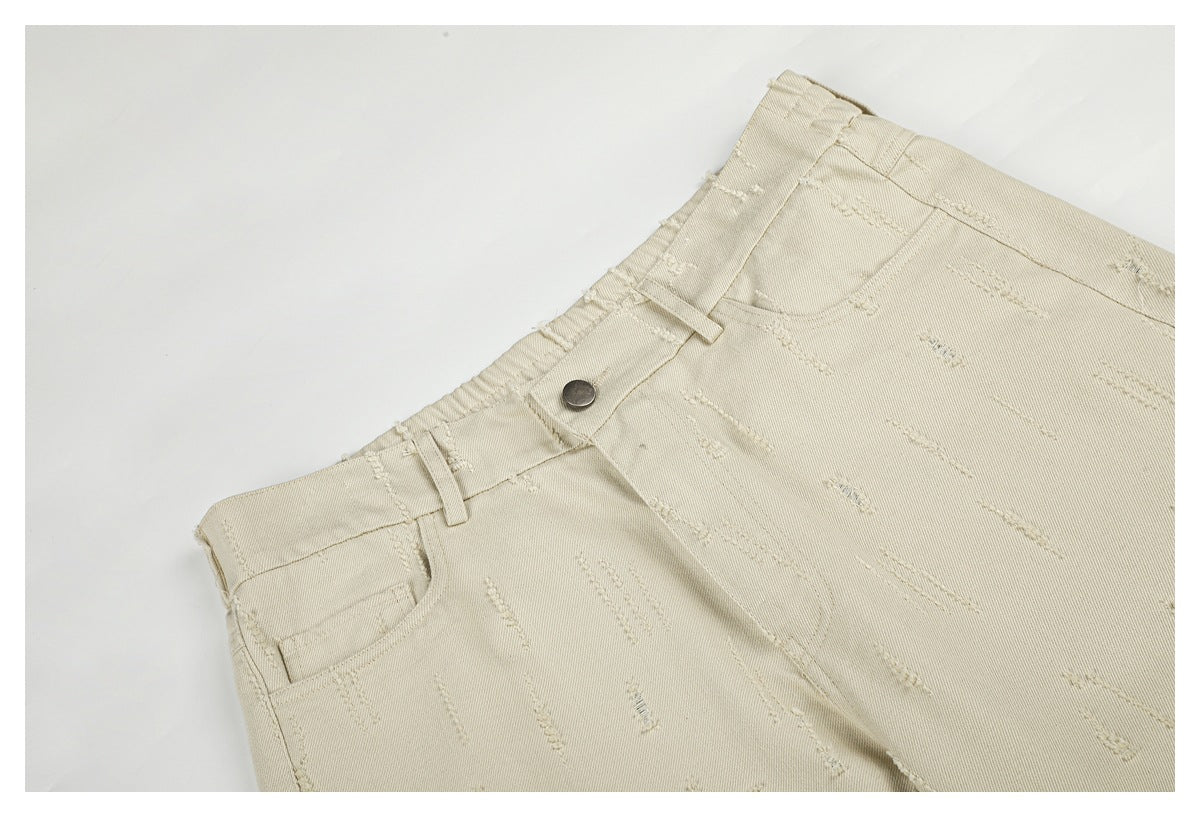 Close-up of cream trousers showing the waistband, metal button, front pocket and scattered raised stitch marks.