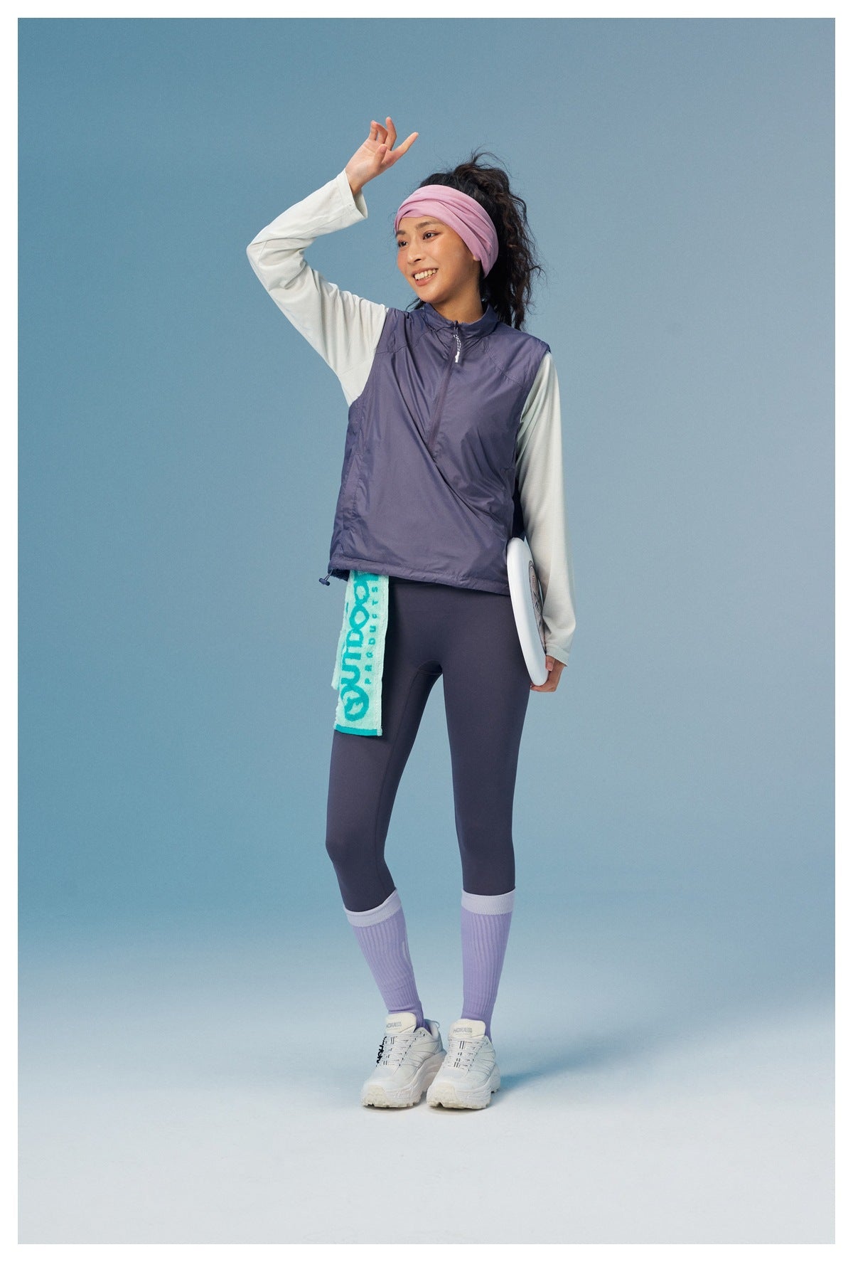 Full-length model wearing a lavender quarter-zip vest, white top, dark leggings, and lavender socks.