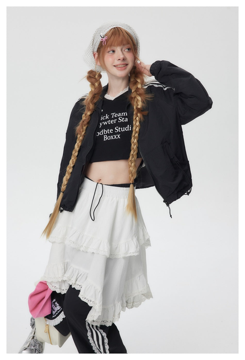 Model wearing an open black jacket over a black printed crop top and a white tiered lace skirt.