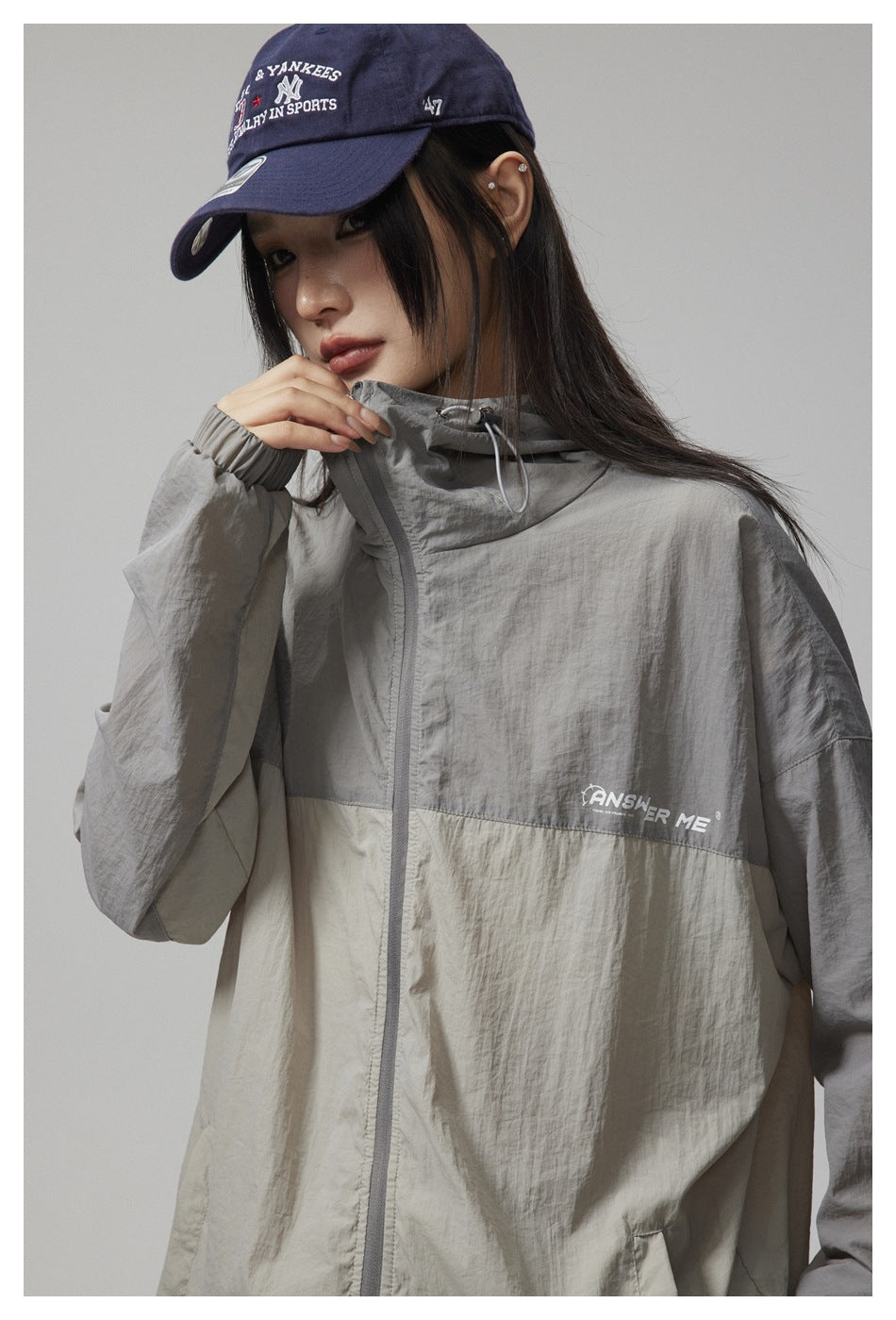 Model wearing a gray and light beige color-block hooded zip jacket with a chest logo.