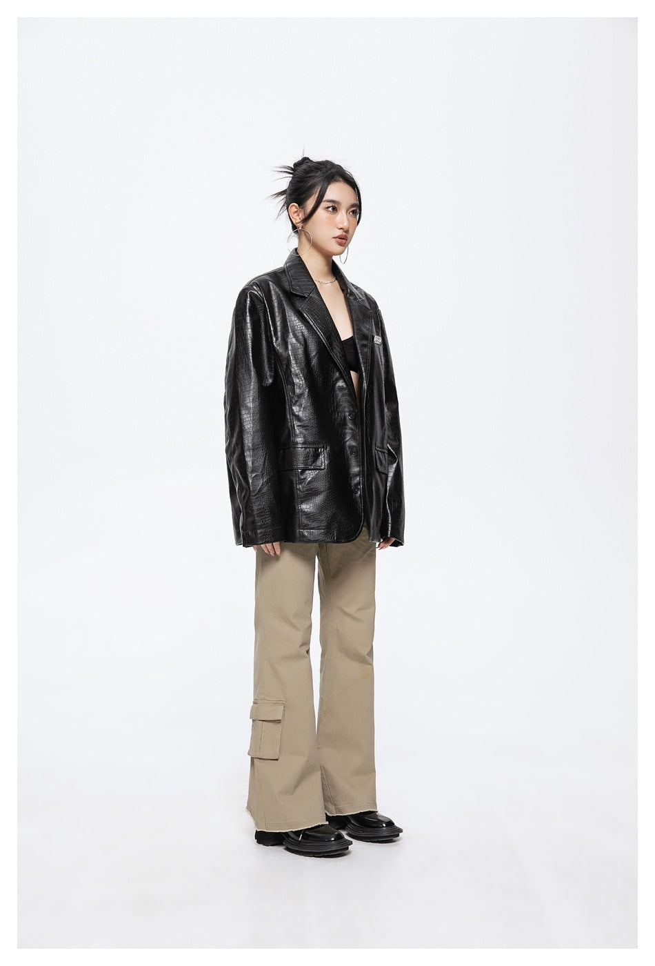 Three-quarter view of a model in a black crocodile-textured blazer and beige cargo trousers.