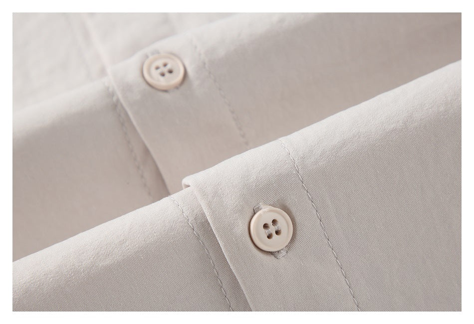 Close-up of two light beige buttons and stitched placket on a pale garment.