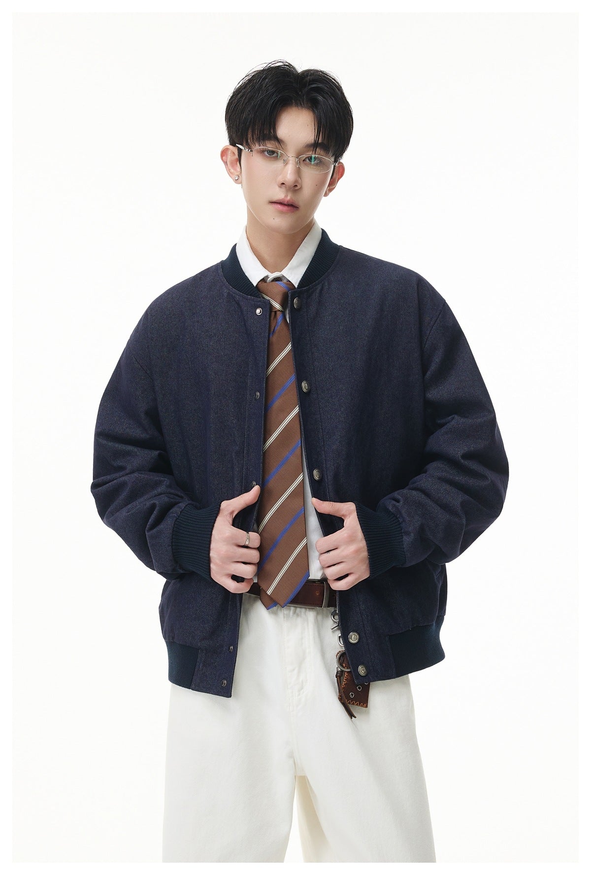 Front view of a model wearing a dark navy rib-trimmed snap jacket, white shirt, striped tie, and white trousers.