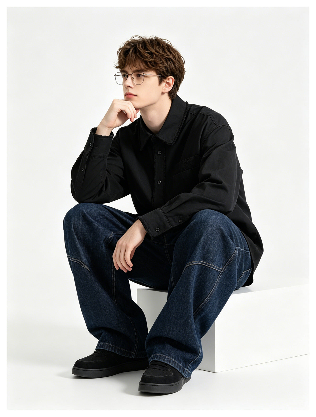 Seated model wearing a black long-sleeve button-up shirt with a chest pocket and dark jeans.
