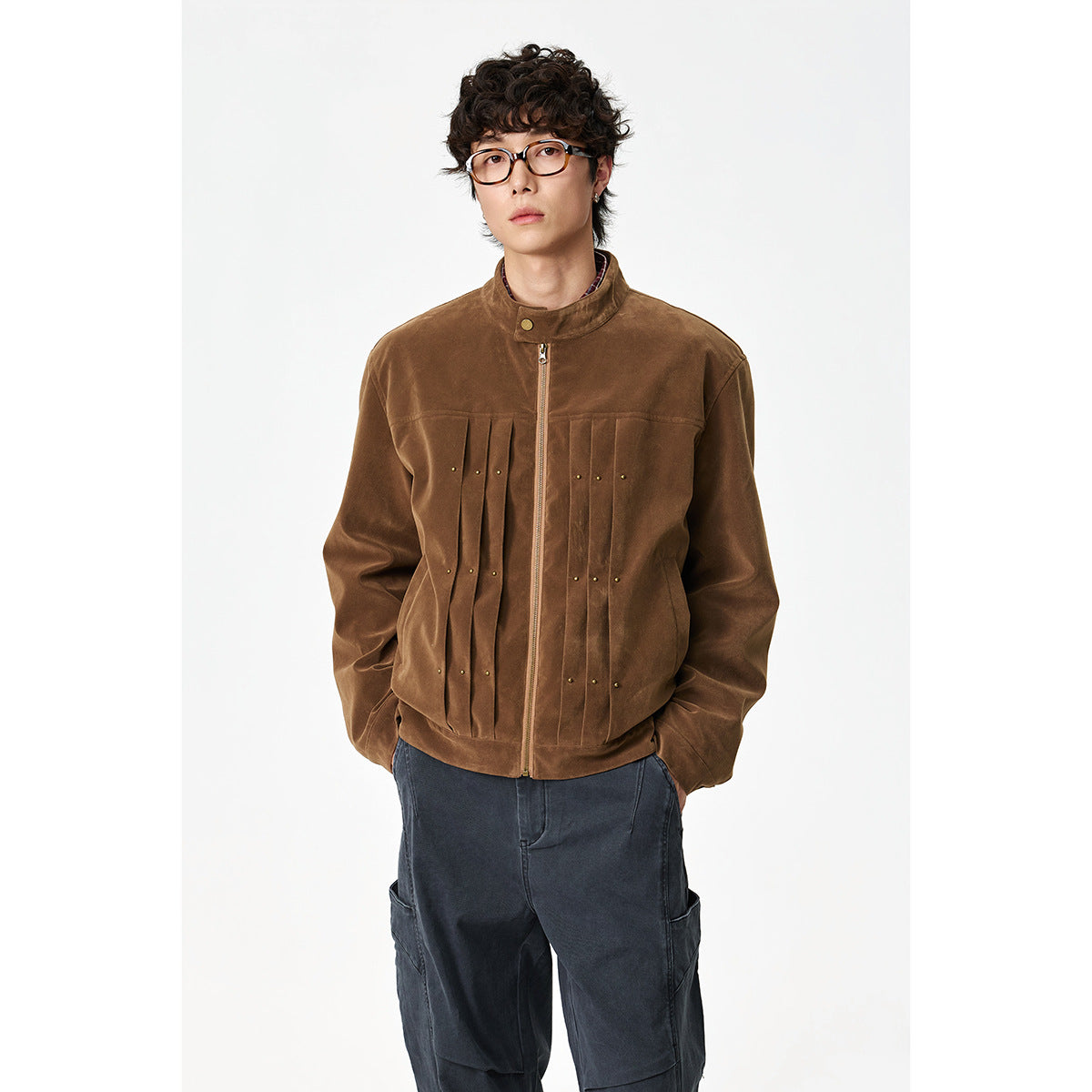 Front view of a model wearing a brown stand-collar zip jacket with pleated front panels and small brass studs.