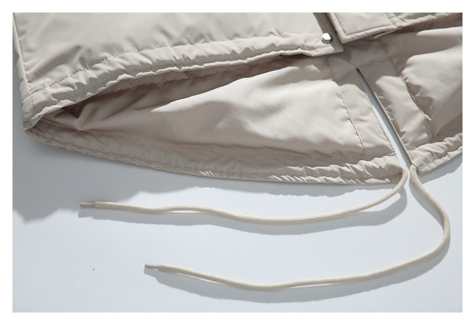 Close-up of a light beige jacket hem with an adjustable drawcord and metal snap.