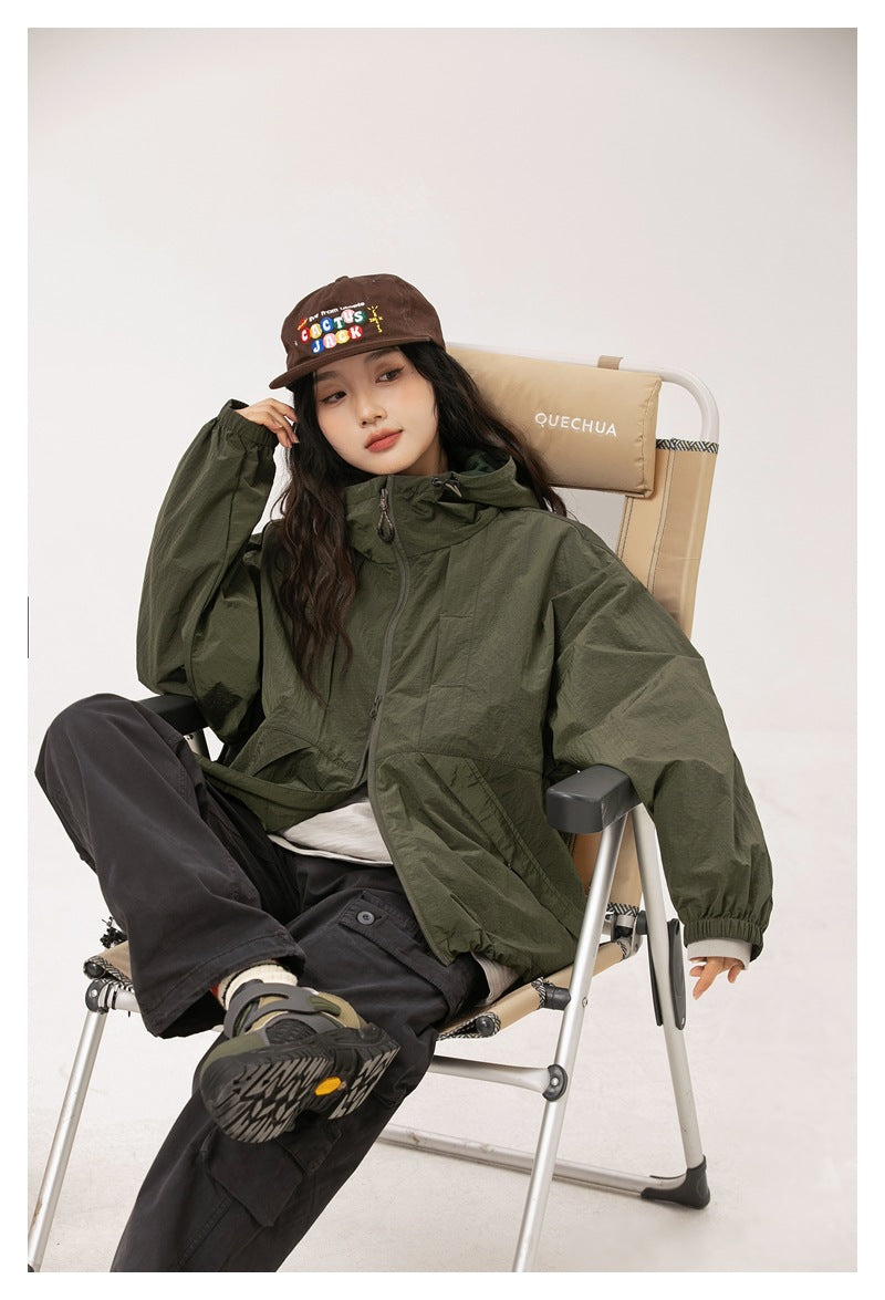 Seated model wearing a zipped olive-green hooded jacket with elastic cuffs.