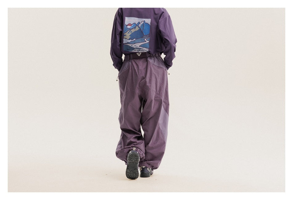 Rear view of a model in loose plum-purple pants and a purple top with a colorful mountain graphic.