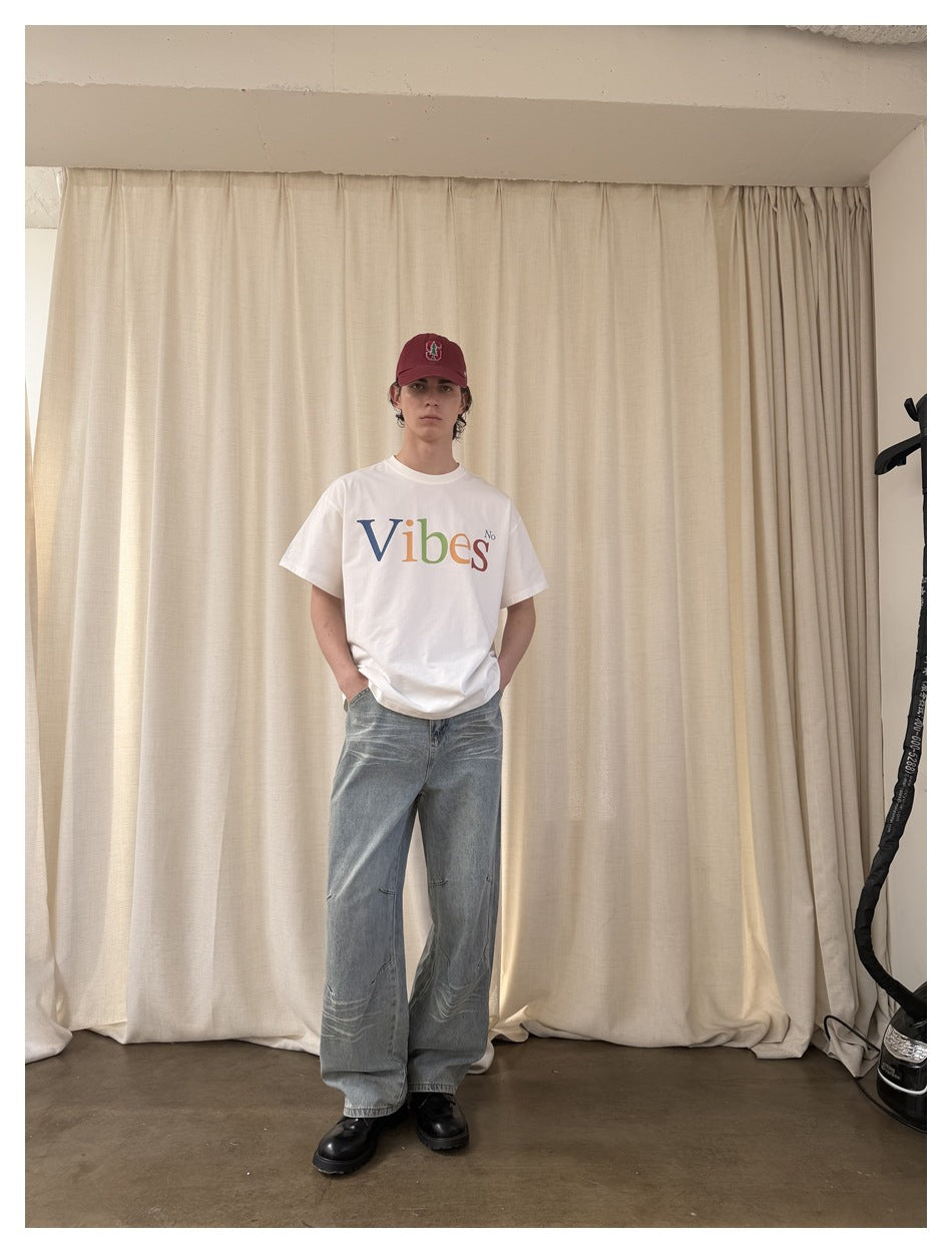 Full-length front view of a model wearing a white “Vibes No” graphic T-shirt and loose light-wash jeans.