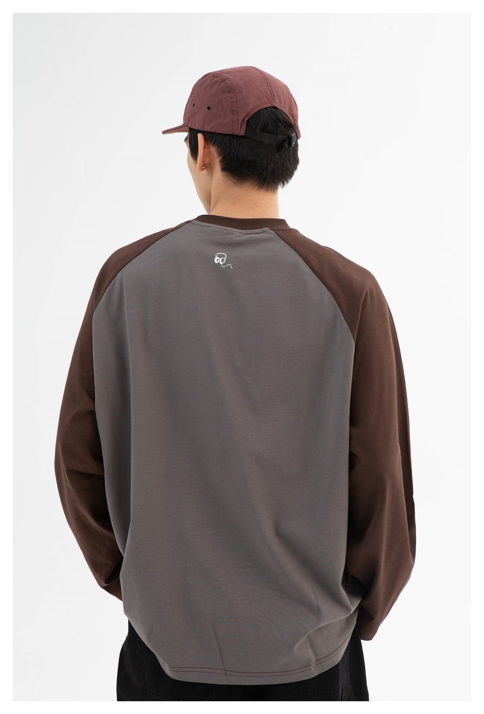 Rear view of a model wearing a brown and gray color-block long-sleeve shirt and burgundy cap.