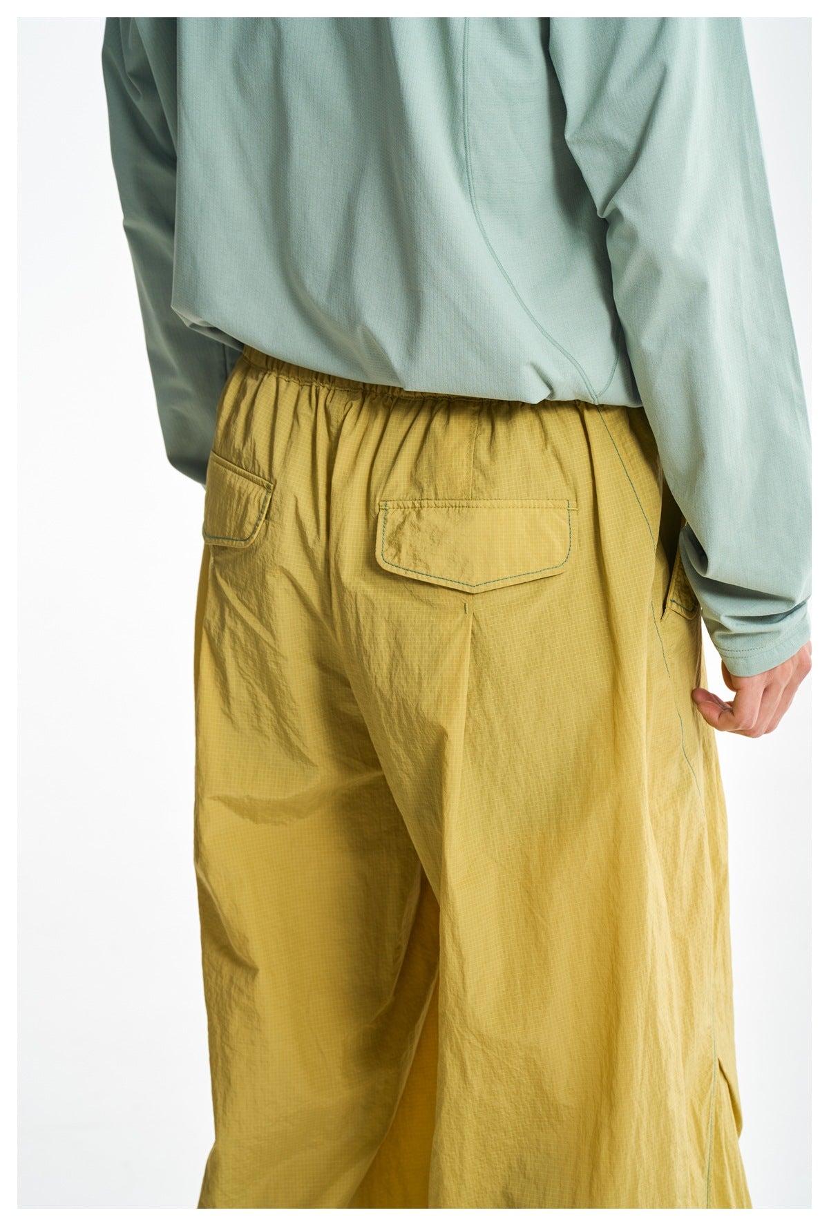 Close-up of the back of mustard-yellow pants, showing the elastic waistband and two flap pockets with contrast stitching.
