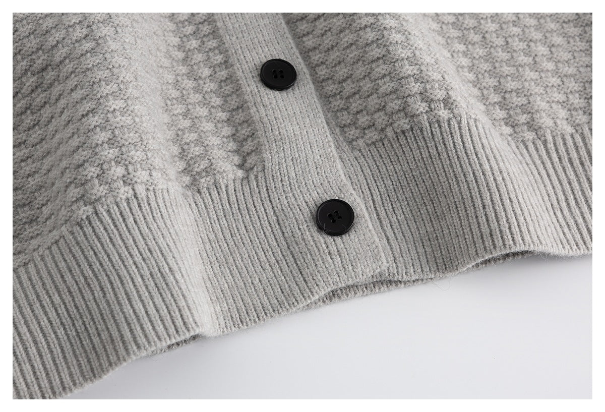 Close-up of the ribbed hem and black buttons on a light gray knit cardigan.