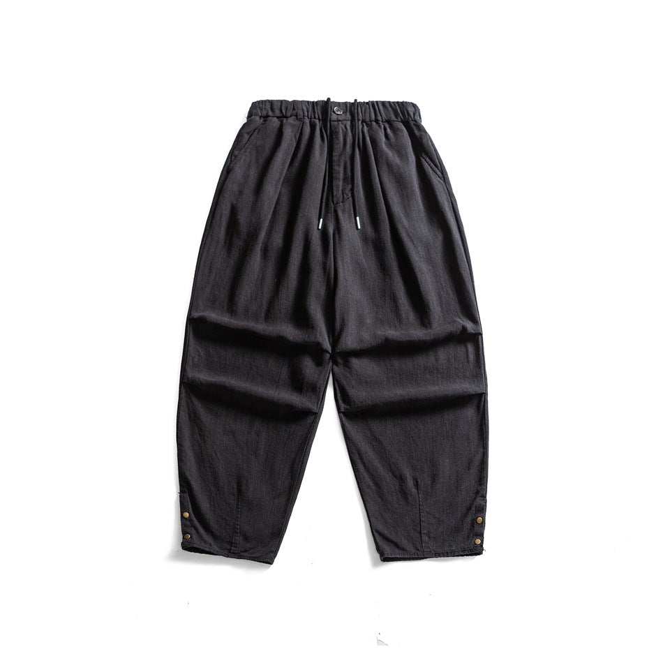 Black wide-leg linen-look pants flat lay with elastic drawstring waist, side pockets and snap buttons at hems