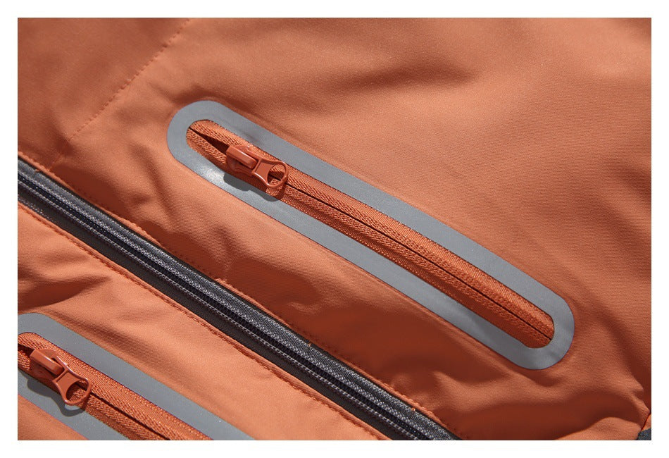 Close-up of rust-orange jacket pockets with orange zippers and gray reflective-looking borders.