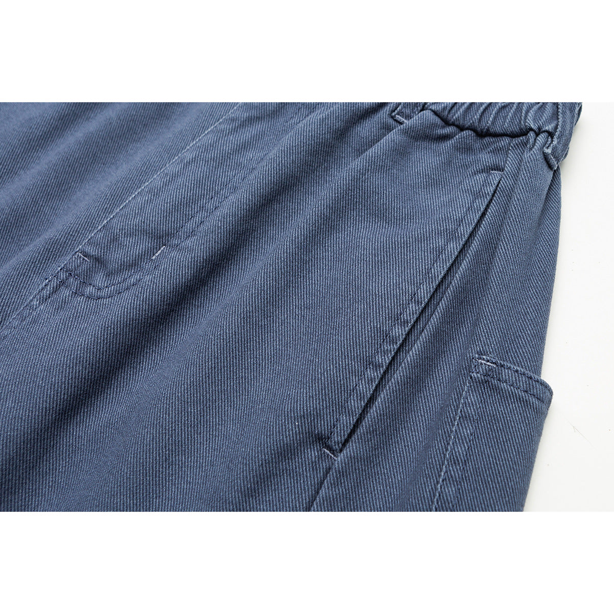 Close-up of blue trousers showing the elastic waistband, stitching, and side pocket.