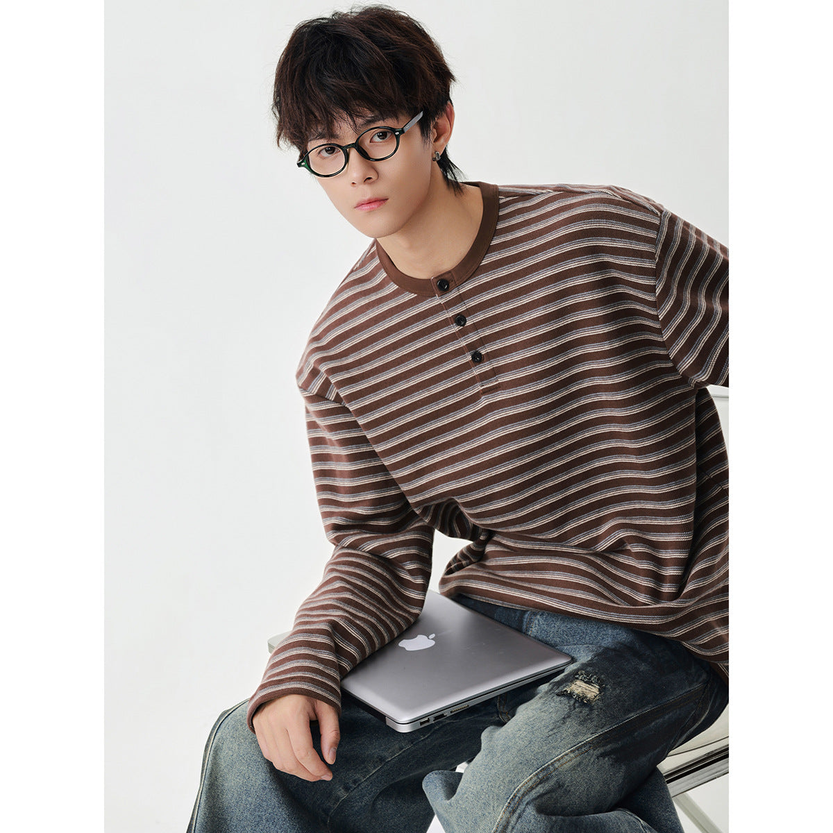 Seated model wearing a brown striped long-sleeve henley with a three-button placket.