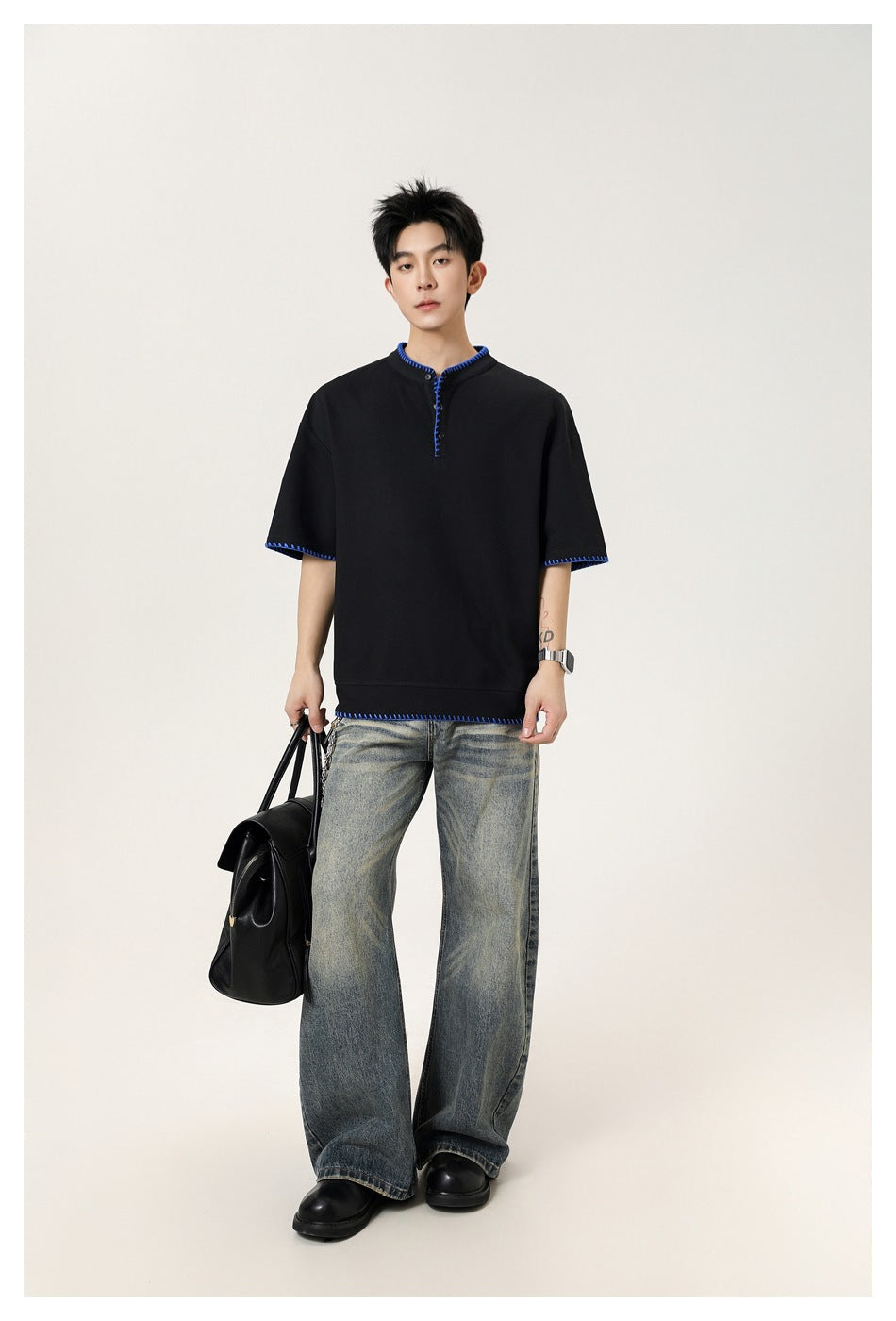 Full-length model wearing a black short-sleeve shirt with blue contrast stitching and wide-leg jeans.