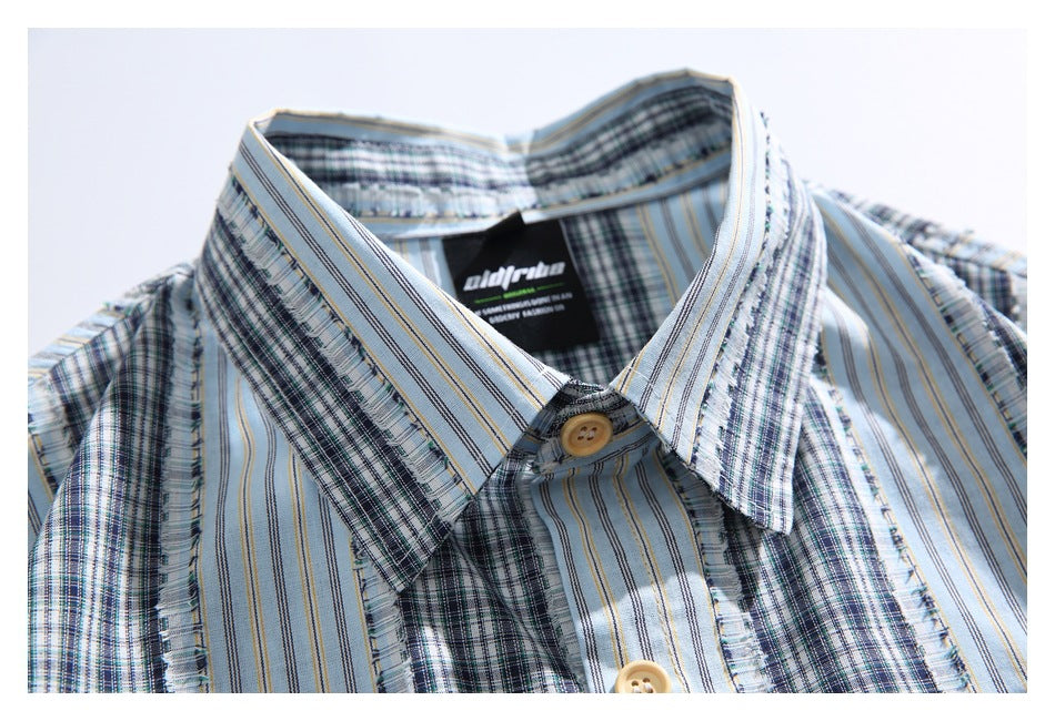 Close-up of the shirt collar and upper front, showing pale blue striped and plaid panels and tan buttons.