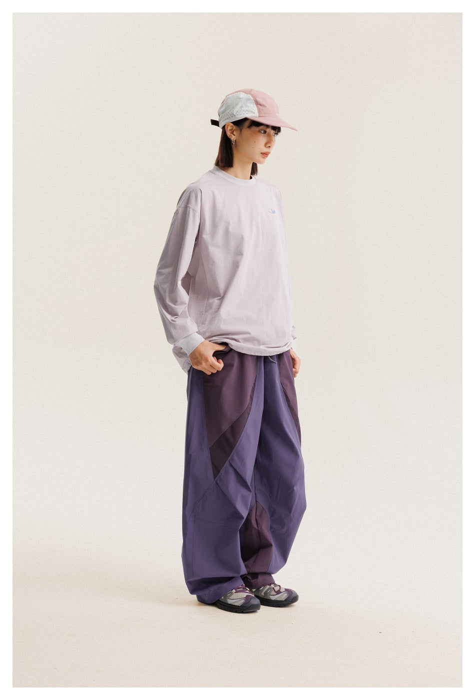 Model in a pale lilac long-sleeve shirt and loose purple paneled pants, shown in side profile.