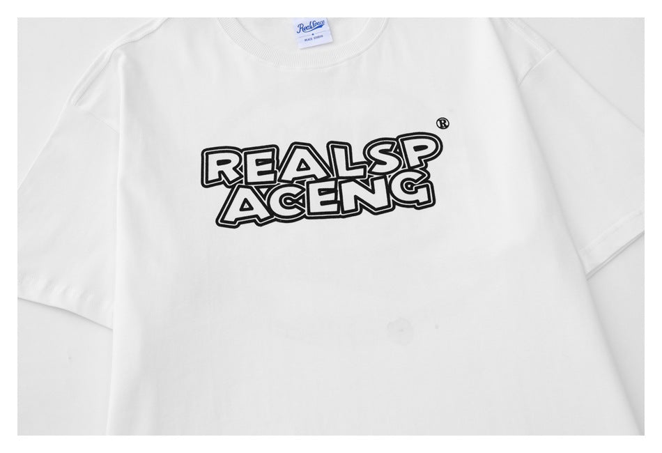 Close-up of a white T-shirt front with bold black outlined “REALSP ACENG” lettering and a small neck label.