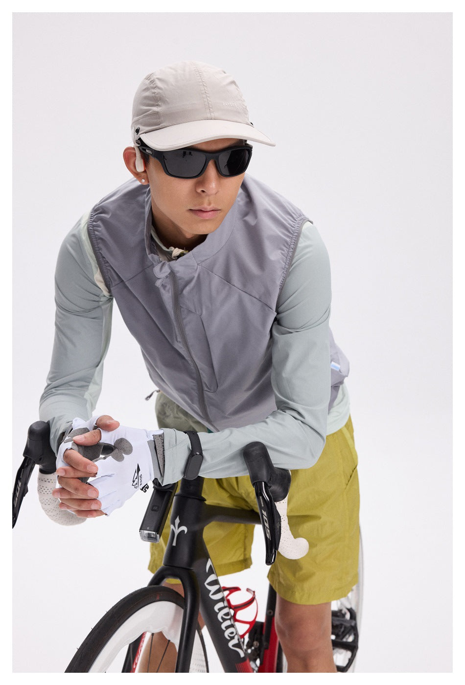 Close view of a cyclist wearing a gray zip-front vest over a pale mint long-sleeve shirt and mustard-yellow shorts.