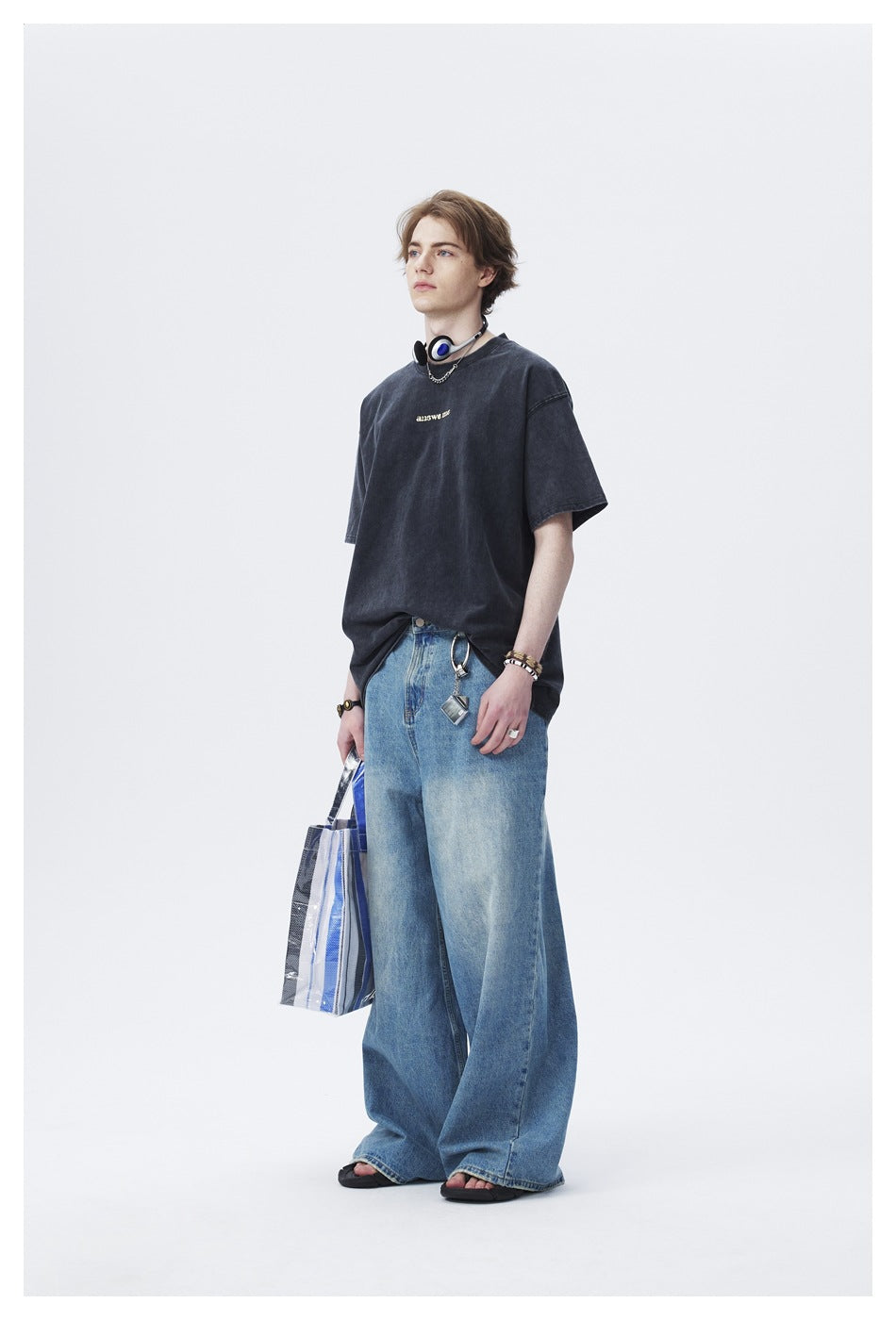 Full-length model wearing a dark oversized graphic T-shirt, wide-leg blue jeans, and sandals.
