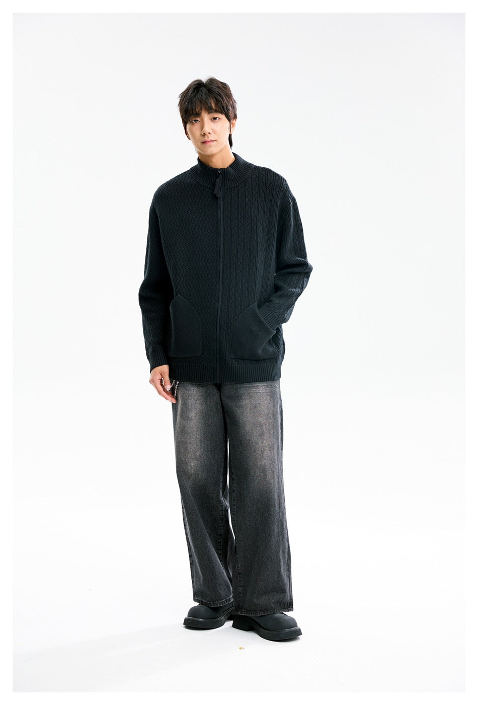 Full-length front view of a model wearing a zipped dark patterned cardigan with a high collar and patch pockets.
