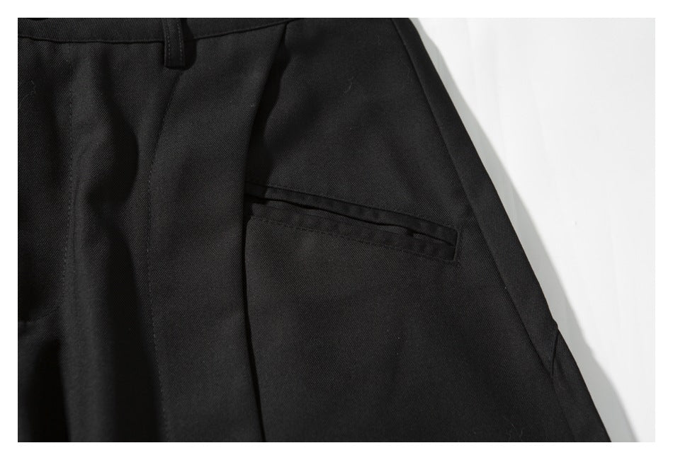 Close-up of black tailored trousers showing a belt loop, seams, and a narrow welt pocket.