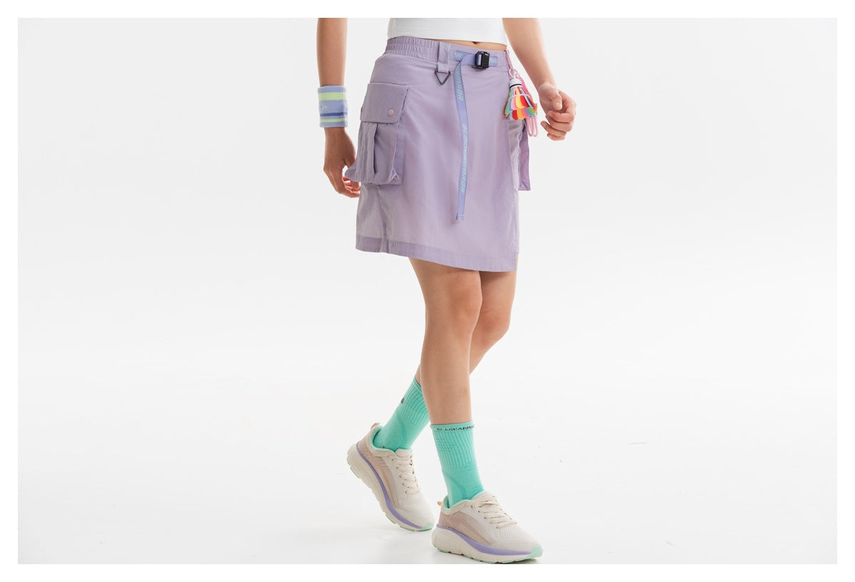 Angled front view of a model wearing a lilac cargo skirt with a black belt, flap pockets and colorful tassel.
