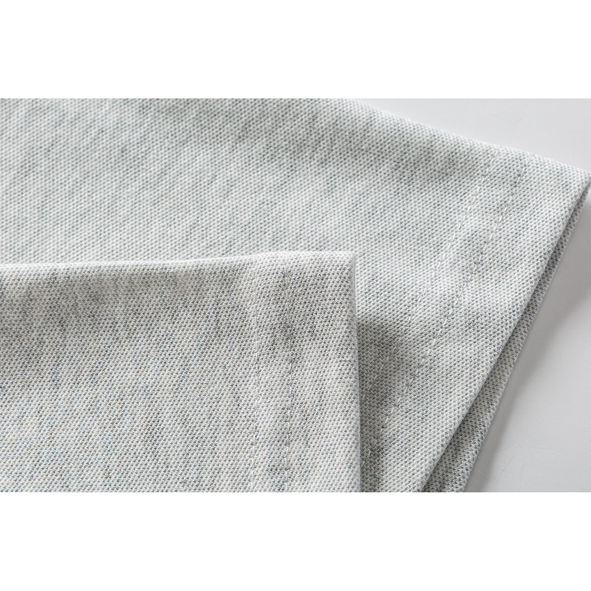 Close-up of the light gray shirt fabric and double-stitched hem.