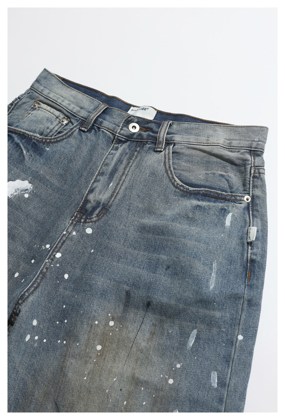 Partial front view of faded blue jeans with five-pocket styling and scattered white paint splatters.