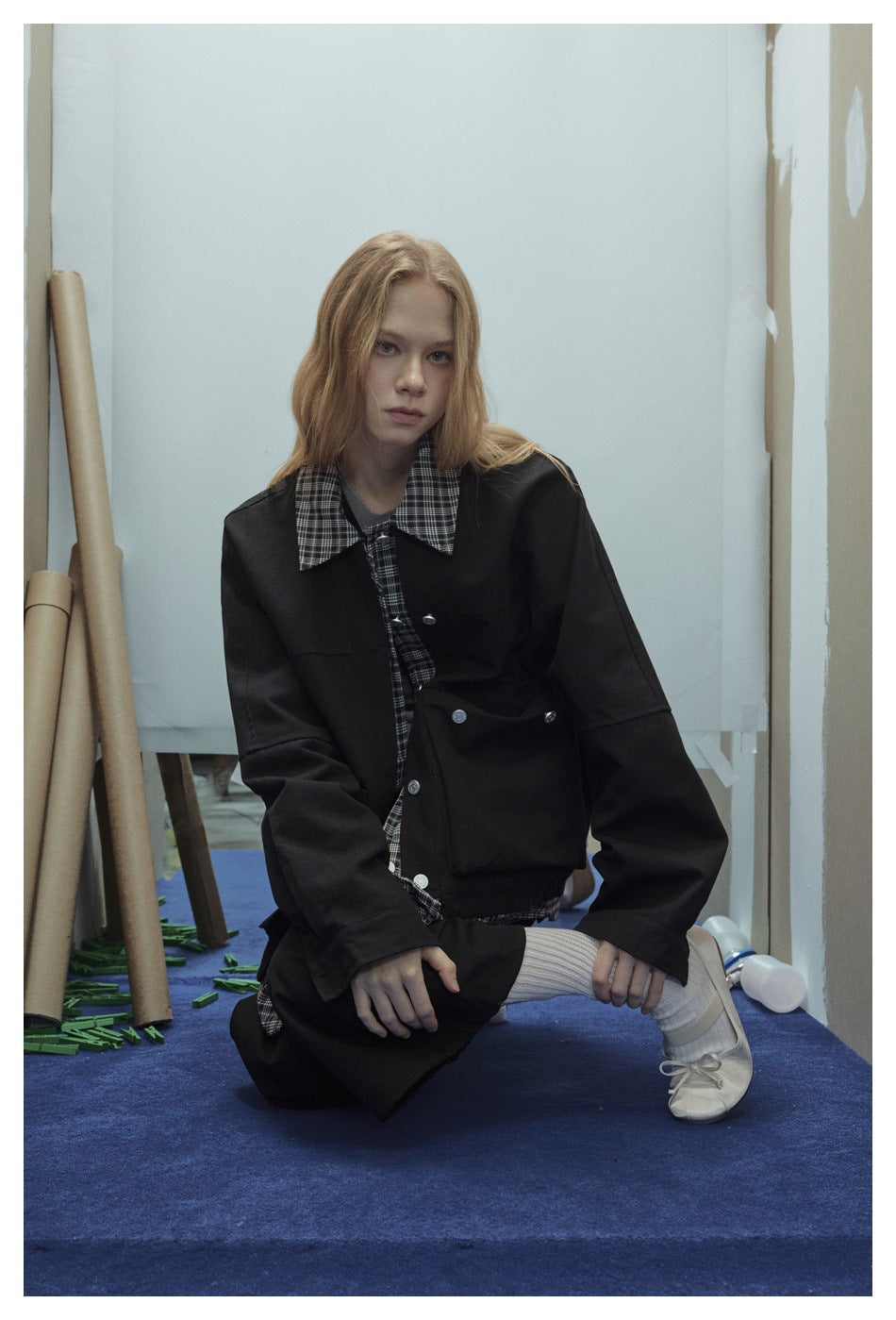 Model wearing a black button-front jacket with a black-and-white plaid collar and shirt, paired with loose black trousers.