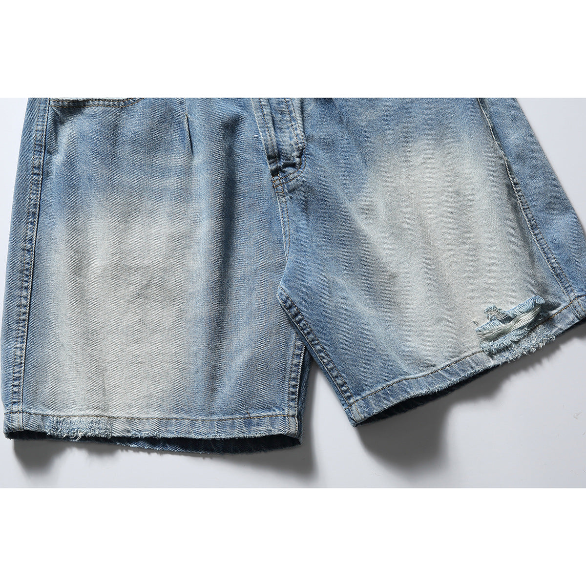 Close-up of faded blue denim shorts with raw hems and a small distressed tear near one leg opening.