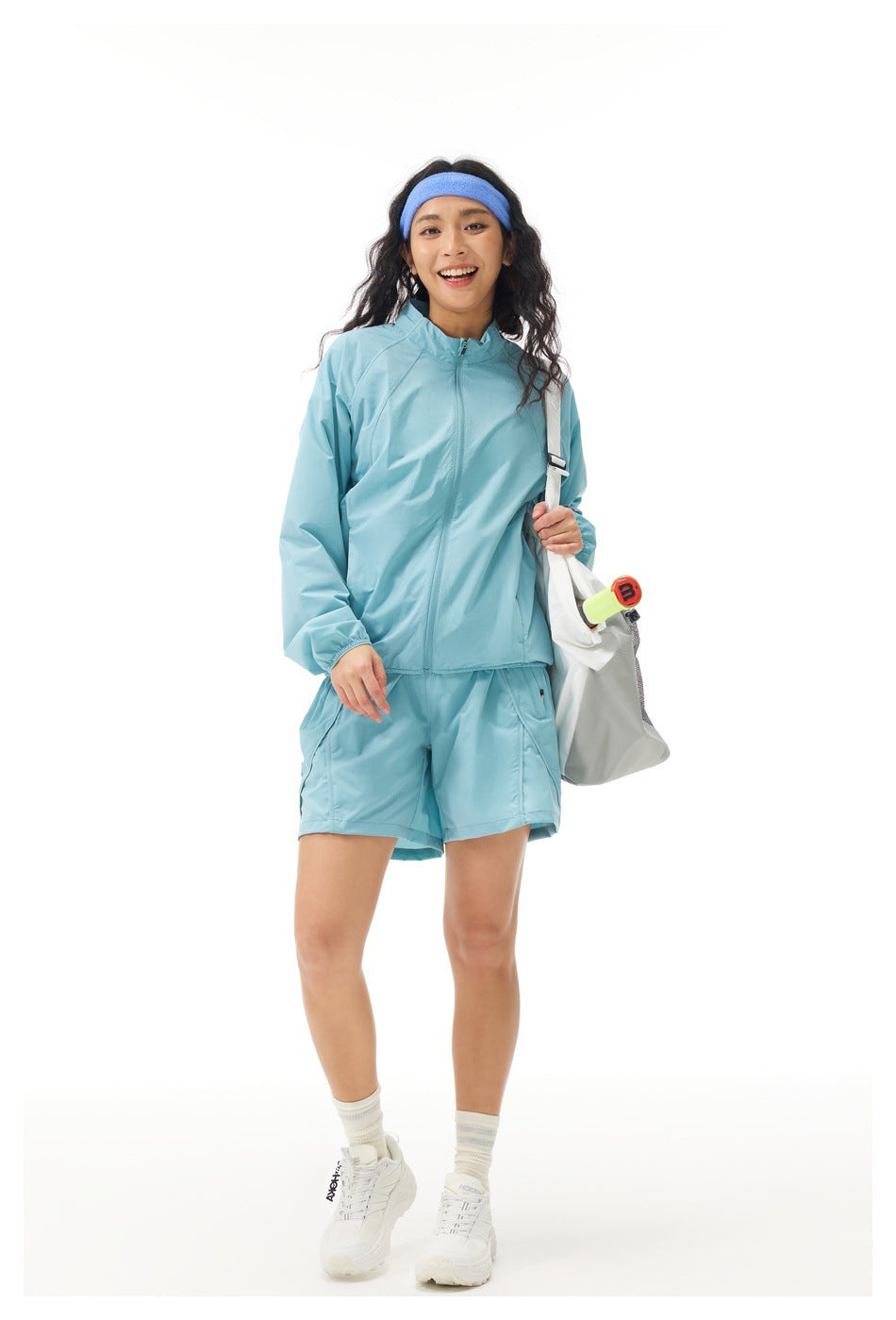 Full-length model wearing a light blue zip jacket and matching shorts with a blue headband and white sneakers.
