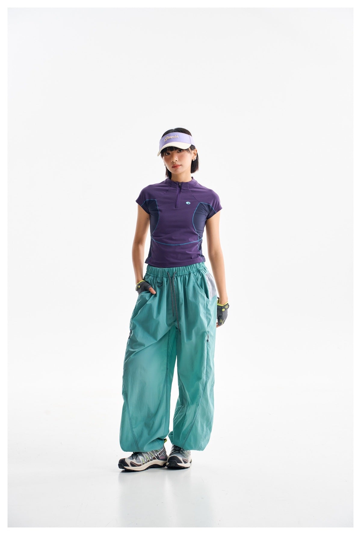 Front view of a model wearing a purple zip-neck top with teal panels and loose teal pants.