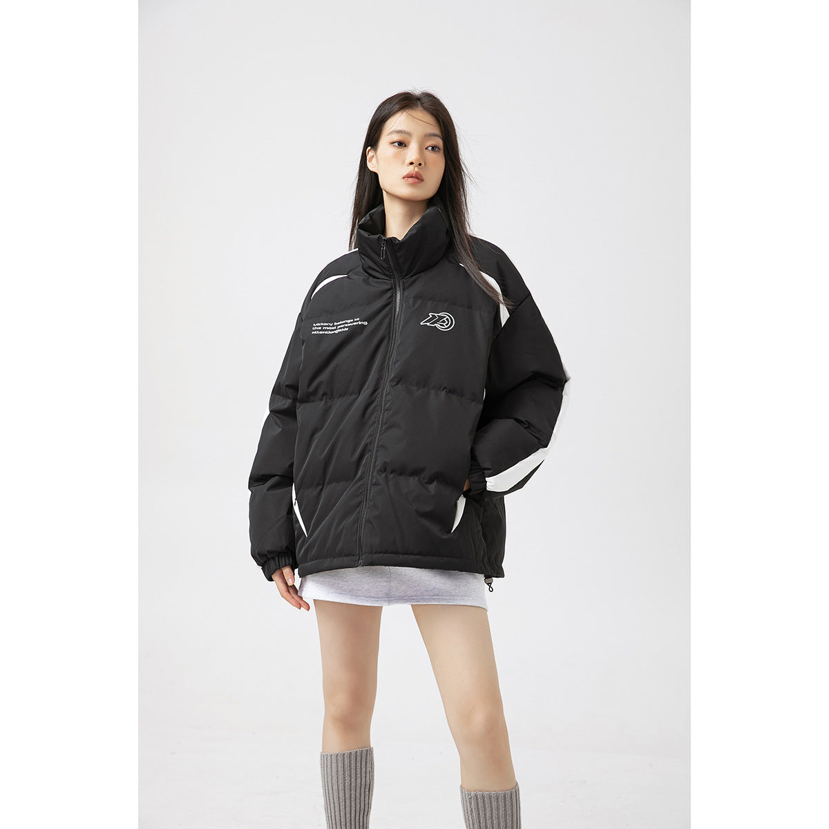 Front view of a model wearing a black padded zip jacket with a high collar, white sleeve panels and chest graphics.