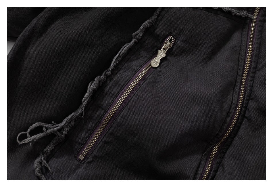 Close-up of a black jacket showing a slanted zip pocket with a metal pull and a frayed trim edge.