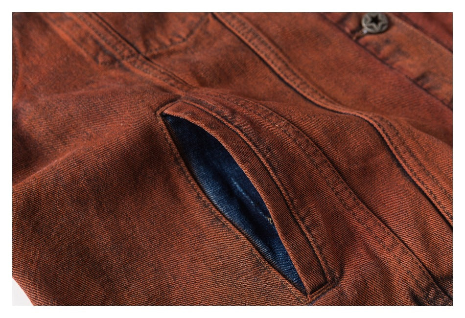 Close-up of a rust-red washed denim jacket welt pocket, showing dark blue lining and stitched edges.