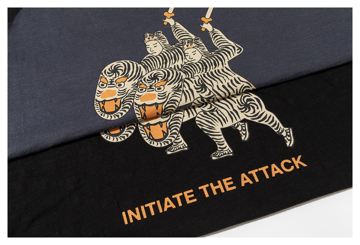 Close-up of black and slate-blue shirts with a graphic of tiger-costumed figures and orange “INITIATE THE ATTACK” text.