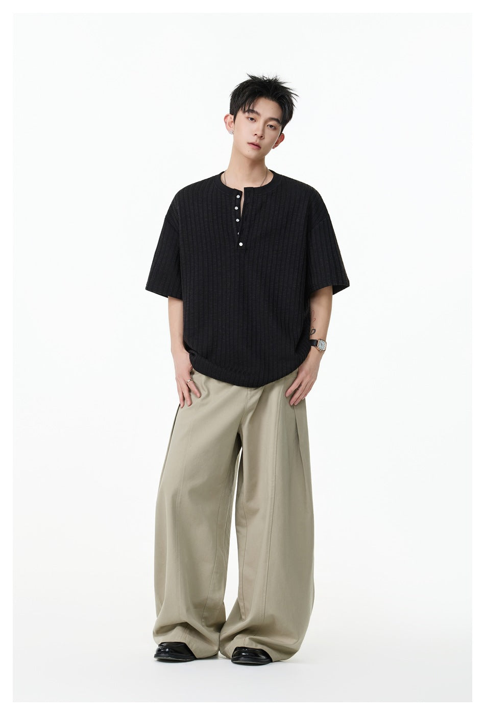 Model wearing a black short-sleeve ribbed Henley shirt with a short button placket and beige wide-leg trousers.