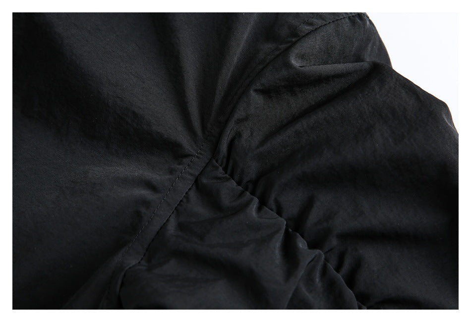 Close-up of stitched seams and gathered black jacket fabric.