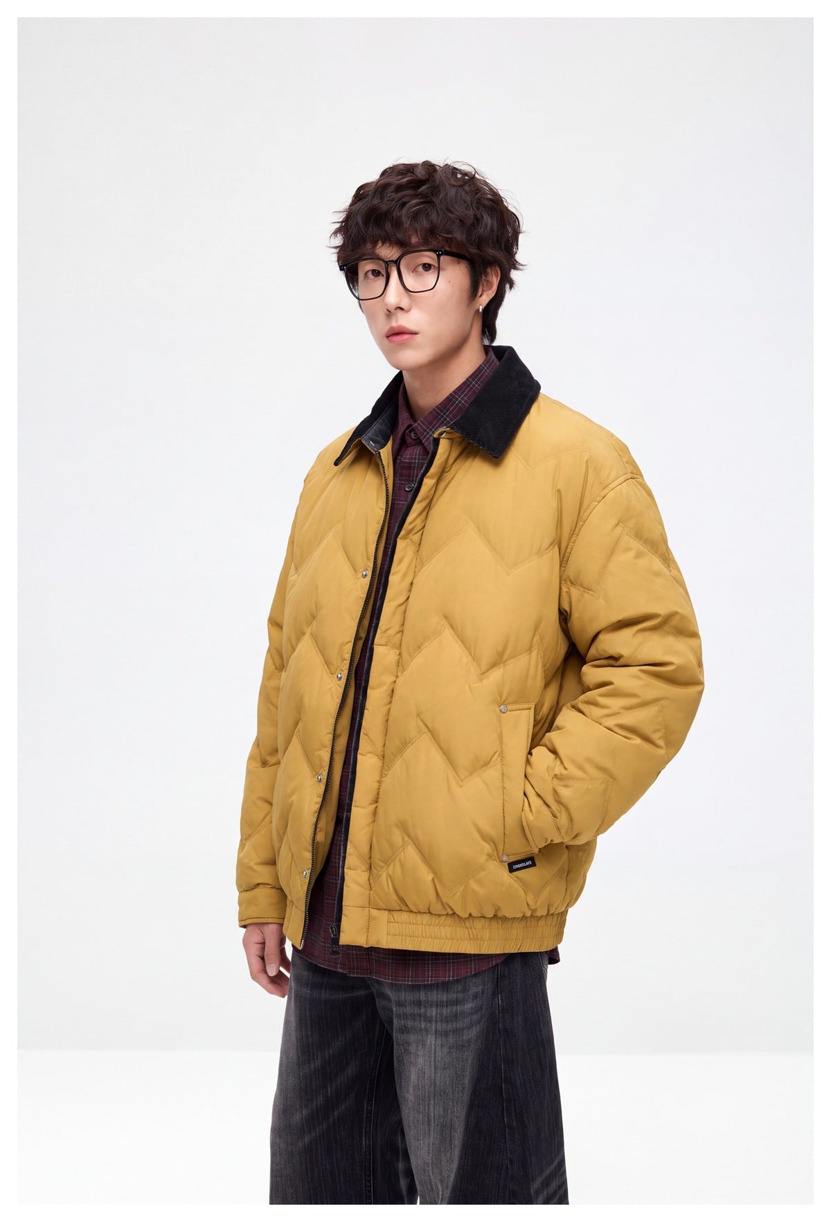 Three-quarter view of a model wearing a mustard-yellow chevron-quilted jacket with a dark collar and front pockets.