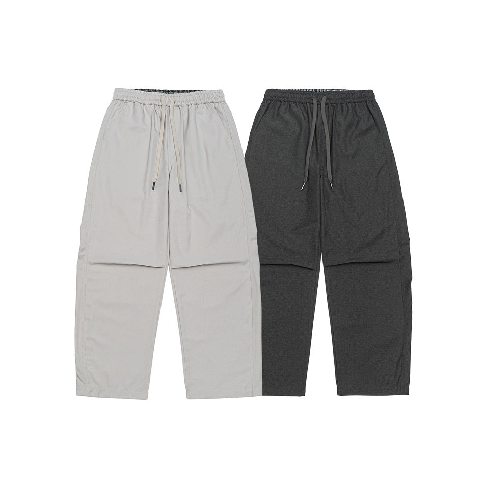 Two pairs of loose drawstring pants laid flat, one light gray and one dark charcoal, front view.