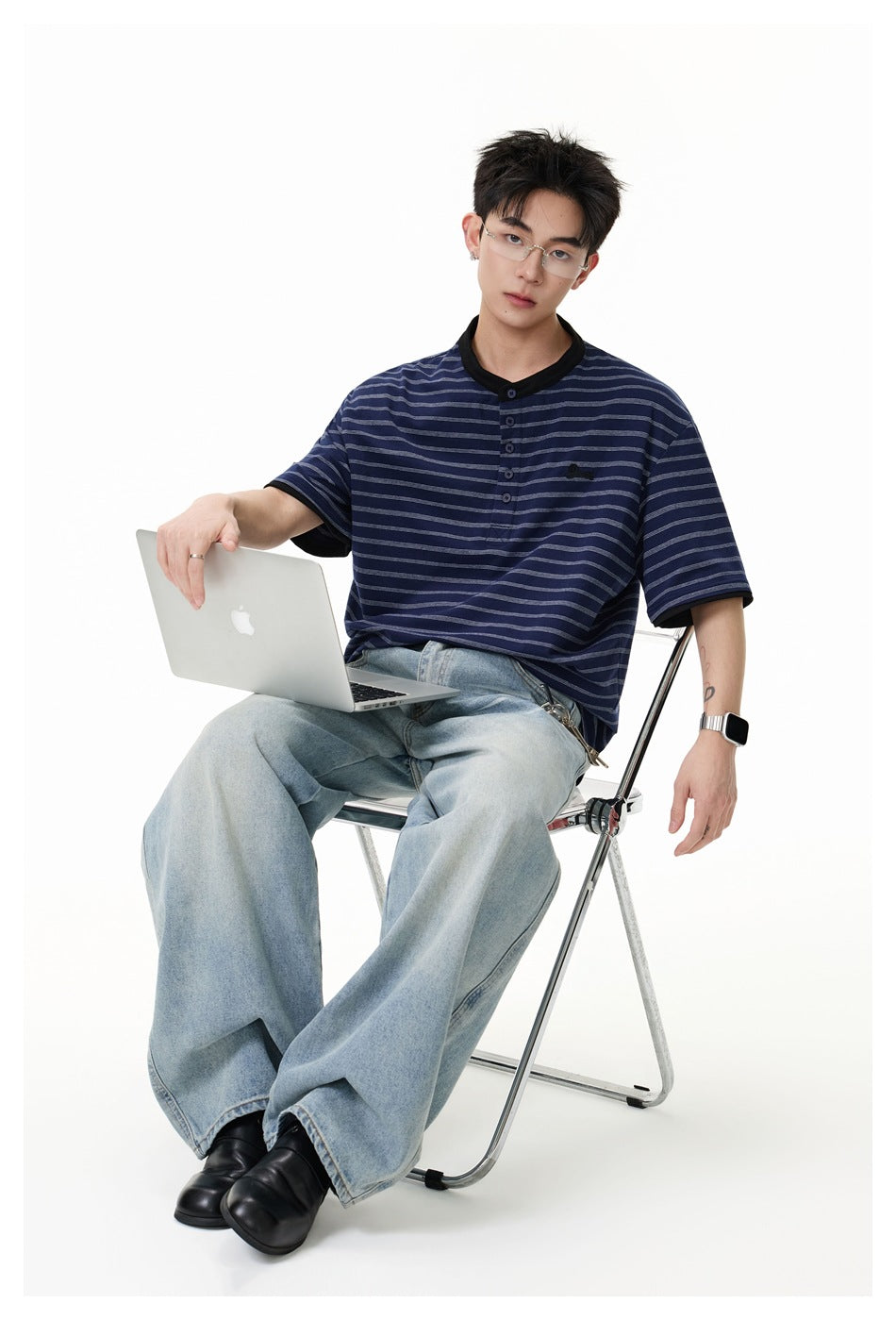 Seated model wearing a navy striped short-sleeve henley with black trim and loose light-wash jeans.