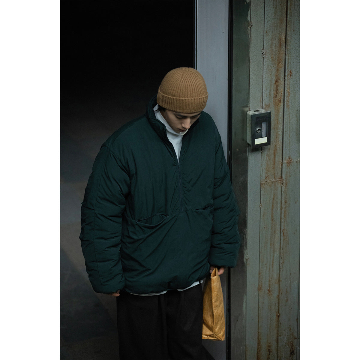 Closer view of a model wearing a dark teal padded pullover jacket with a high collar and front pocket.